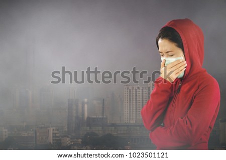 Woman with flu sneezing, woman dressed pink in winter clothing wearing mask to her nose in a cold and flu health concept against 