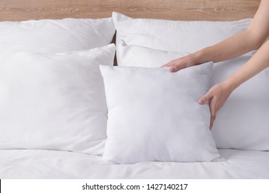 Woman Fluffing Soft Pillows On Bed