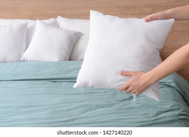 Woman Fluffing Soft Pillows On Bed