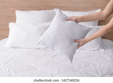 Woman Fluffing Soft Pillows On Bed