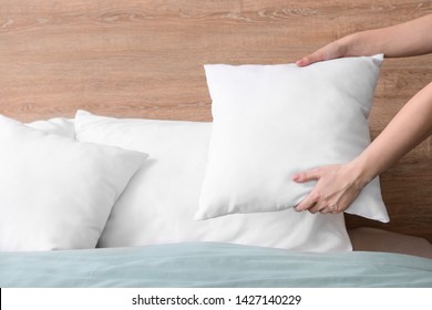 Woman Fluffing Soft Pillows On Bed