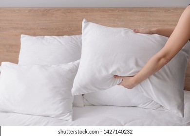 Woman Fluffing Soft Pillows On Bed