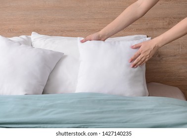 Woman Fluffing Soft Pillows On Bed