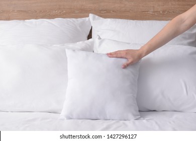 Woman Fluffing Soft Pillows On Bed