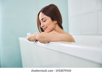 Woman folding arms on a hot tub and placing her chin on them while sitting with closed eyes and smile