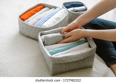 Woman folding clothes, organizing stuff in boxes and baskets. Concept of minimalism lifestyle and japanese t-shirt folding system. Minimalist storage, capsule wardrobe concept