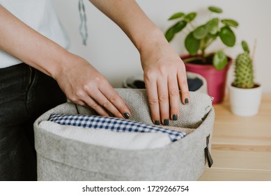 Woman folding clothes, organizing stuff in basket. Concept of clothes storage, minimalism lifestyle and japanese t-shirt folding system. Tidy up in wardrobe