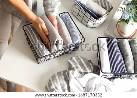 A woman folds her clothes and puts them in metal black baskets and boxes. Nordic style minimalism.