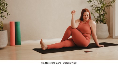 Woman following instruction on cellphone while doing yoga. Female watching the mobile phone while practicing yoga stretching workout. - Powered by Shutterstock