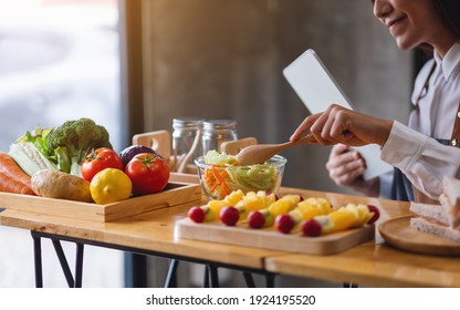 A Woman Following Recipe On Digital Tablet While Cooking Salad And Sandwich In The Kitchen, Online Learning Cooking Class Concept