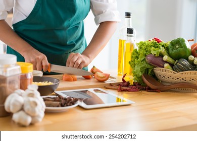 Woman Following Recipe On Digital Tablet And Cooking Healthy Meal