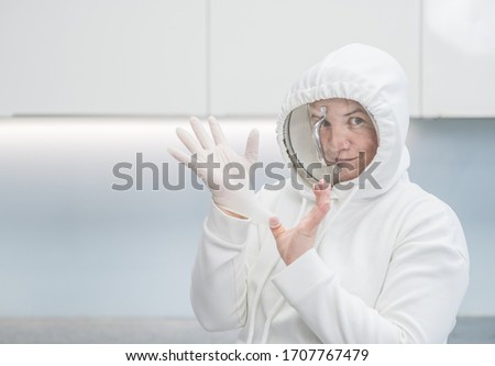 Woman fooling around at home during coronavirus quarantine, dressed up in a funny protective suit with a pan cover and latex gloves