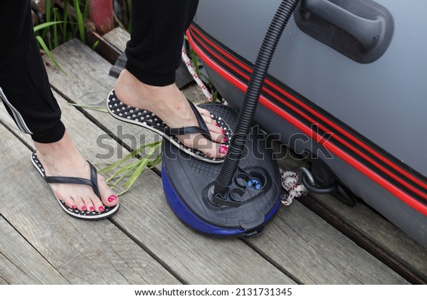 A woman foot pumps up with air\
pump an inflatable boat closeup on old wooden Pier before\
trip