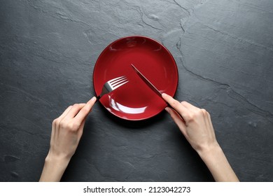 Woman with fork, knife and empty plate at black table, top view