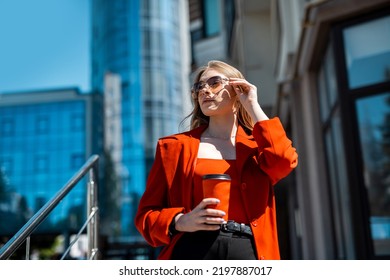 A Woman In A Formal Black Suit Enjoying A Sunny Day And Walking Near The Skyscrapers During A Work Break With A Drink In Her Hand. The Concept Of The Work Of A Woman In The Office