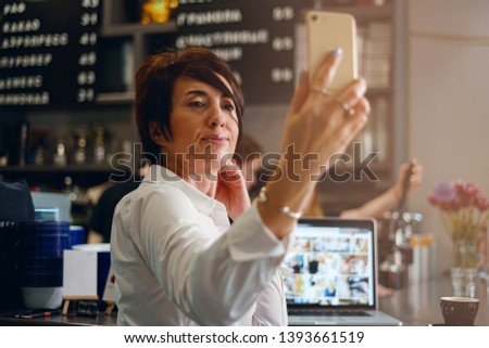 a woman for forty years writes the vlog into the phone while sitting at the bar in a cafe