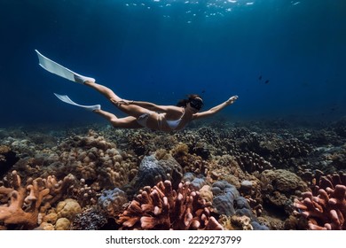 Woman freediver glides with fins over corals. Freediving in deep blue ocean - Shutterstock ID 2229273799