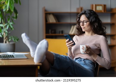 Woman freelance writer rest or procrastinate at workplace. Businesswoman in eyewear distracted from work on laptop scrolling social media on smartphone. Freelancer holding mobile phone and browsing - Powered by Shutterstock