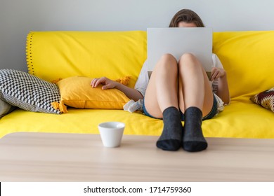 Woman freelancer sitting on the couch with laptops in the socks and putting legs on the table. Work at home. Concept. Cup coffee. Relax at home. 