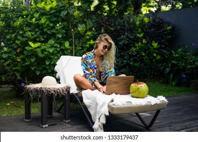 Woman Freelancer, Travel Blogger Works On A Laptop. Sitting On A Lounger In The Garden By The Pool.