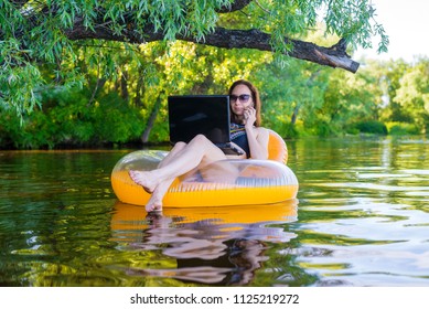 Woman Freelancer Working On A Laptop Sitting In An Inflatable Ring, Remote Work. Woman Workaholic.