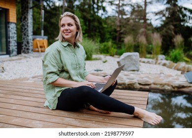 Woman, freelancer working on laptop, sitting on a pier by the backyard lake, a concept of remote office, work during vacation. - Powered by Shutterstock