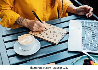 Woman freelancer writing numbers in notepad while working with laptop in street cafe. Time Management