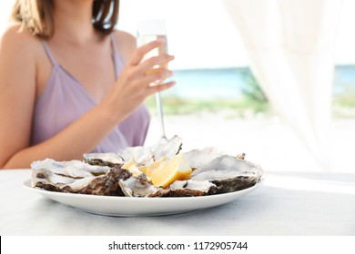 Woman with fresh oysters and glass of champagne at table
