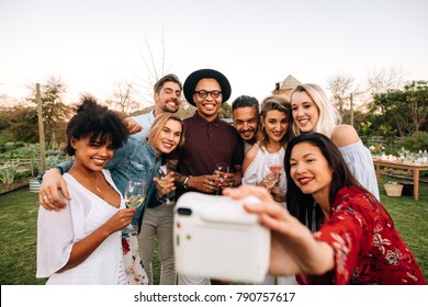 Woman With Friends Taking Selfie Using Instant Camera. Group Selfie At Outdoor Party.