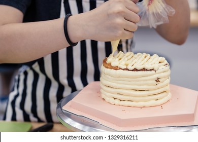 Woman frosting a cake on a rotating turntable with buttercream using a piping bag.
