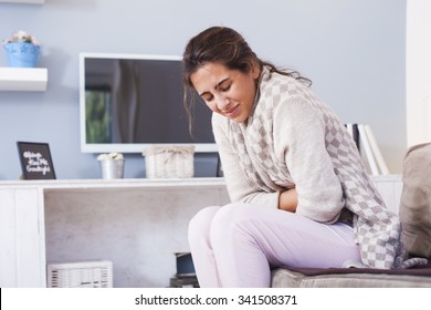 Woman frowning having stomachache sitting on the couch