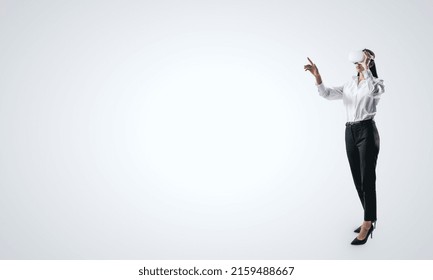 Woman full length standing and working in virtual reality environment in VR glasses, presses by her finger on virtual interface on white backdrop. Innovate and future technology concept, mock up - Powered by Shutterstock