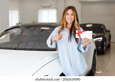 Woman Fun Customer Buyer Client In Shirt Hold Point On Gift Certificate Coupon Voucher Card Store Choose Auto Want Buy New Automobile In Car Showroom Vehicle Salon Dealership Store Motor Show Indoor.