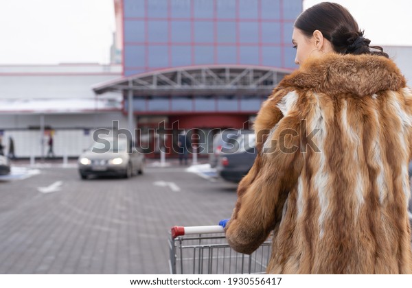 A woman in a fur coat\
goes to a large supermarket with a shopping basket. Winter time of\
the year.