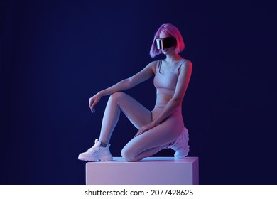 Woman In Futuristic Costume. Female In Modern VR Glasses Interacting With Network While Having Virtual Reality Experience. Augmented Reality Game, Future Technology, AI Concept. VR. Neon Blue Light.