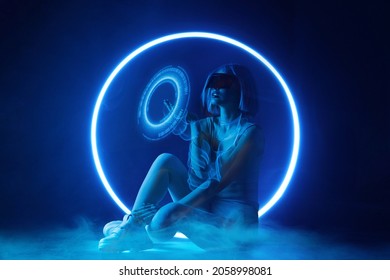 Woman with futuristic tablet in hand. Girl in glasses of virtual reality presses start button. Augmented reality, future technology, AI concept. Holographic interface to display data. Dark background.