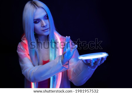 Woman with futuristic tablet in hand. Girl in glasses of virtual reality presses the start button. Augmented reality game, future technology, AI concept. Holographic interface to display data.