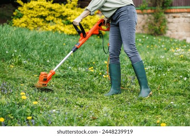 Woman gardener using electric weed trimmer to trim grass in garden. Lawn care in yard - Powered by Shutterstock