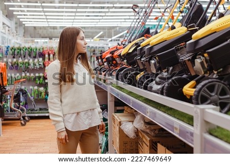 Woman in gardening equipment store chooses gas lawn mower. Purchase of garden equipment