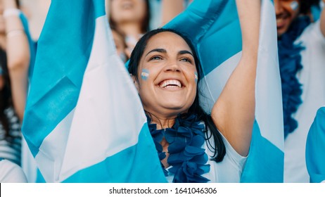 Woman with garland and Argentina flags cheering from stadium fan zone. Argentinian football supporters cheering from stadium. - Powered by Shutterstock