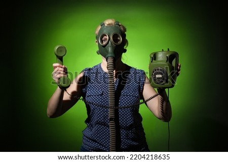 A woman in a gas mask holds a retro phone in her hand on a dark background, hard light.