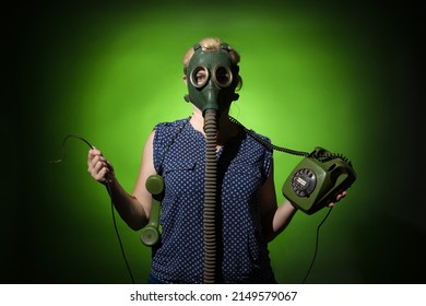 A woman in a gas mask holds torn wires from a retro telephone in her hand on a dark dramatic background, hard light.