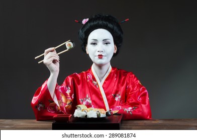 Woman In Geisha Makeup Eating Sushi, Gray Background