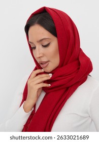 Una mujer toca suavemente su bufanda mientras usa un elegante suéter blanco. La bufanda roja contrasta maravillosamente con su tono cálido de piel, destacando su estilo elegante y aplomo.