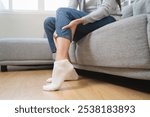 Woman get cramp on the leg sitting on sofa