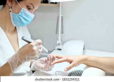  Woman Getting Her Nails Done By A Manicurist In A Beauty Salon. Beautician Holding Nail File And Doing Manicure For A Client. Face Mask And Gloves For Safety.