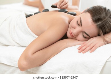 Woman Getting Hot Stone Massage Treatment By Professional Beautician Therapist In Spa Salon. Luxury Wellness, Back Stress Relief And Rejuvenation Concept.