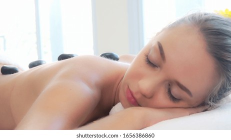 Woman Getting Hot Stone Massage Treatment By Professional Beautician Therapist In Spa Salon. Luxury Wellness, Back Stress Relief And Rejuvenation Concept.