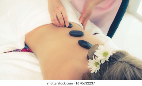 Woman Getting Hot Stone Massage Treatment By Professional Beautician Therapist In Spa Salon. Luxury Wellness, Back Stress Relief And Rejuvenation Concept.