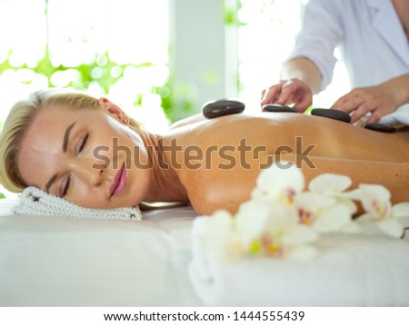 Woman getting hot stone massage treatment by professional beautician therapist in spa salon. Luxury wellness, back stress relief and rejuvenation concept.